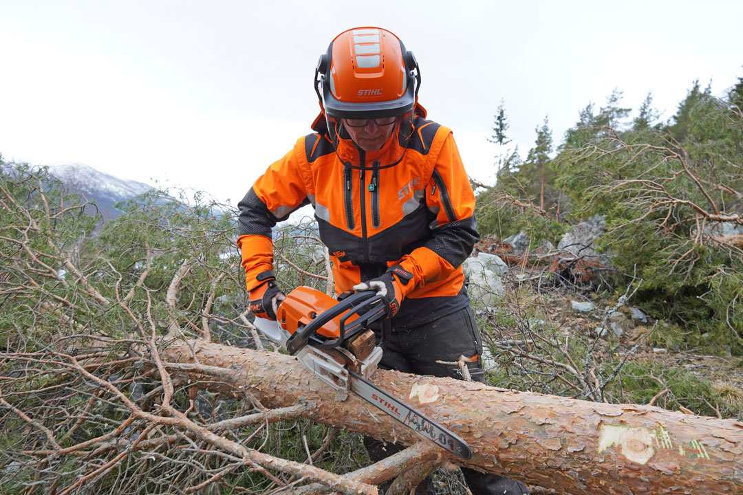 Arbeider i skogen med motorsag iført verneutstyr.