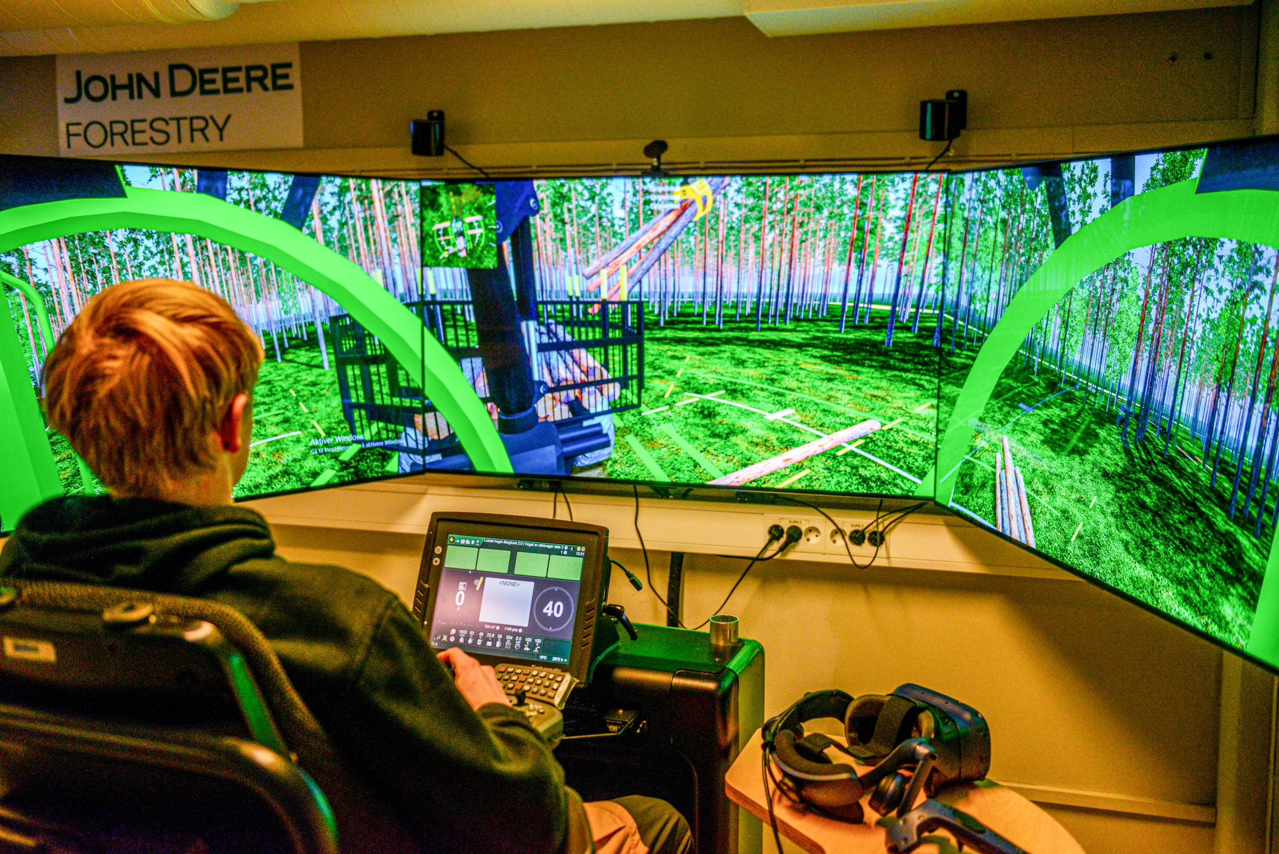 Gutt sitter ved store skjermer i en hogstmaskin-simulator.
