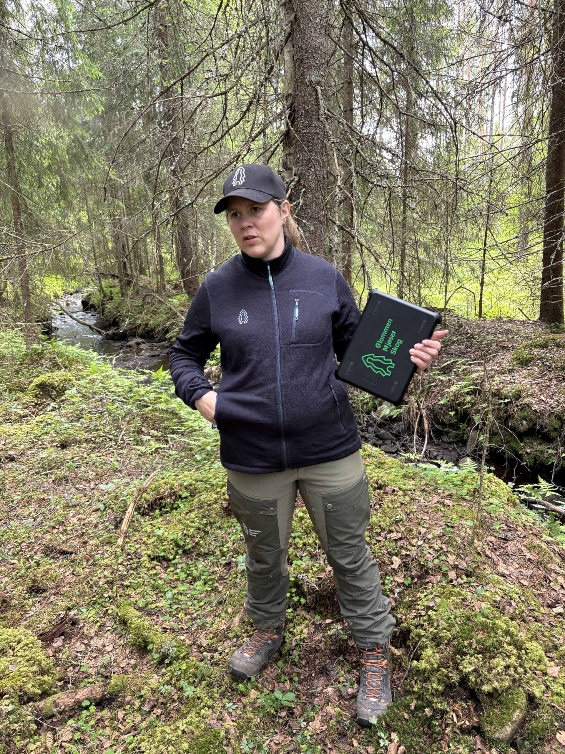 Kvinne ved bekk i skogen.