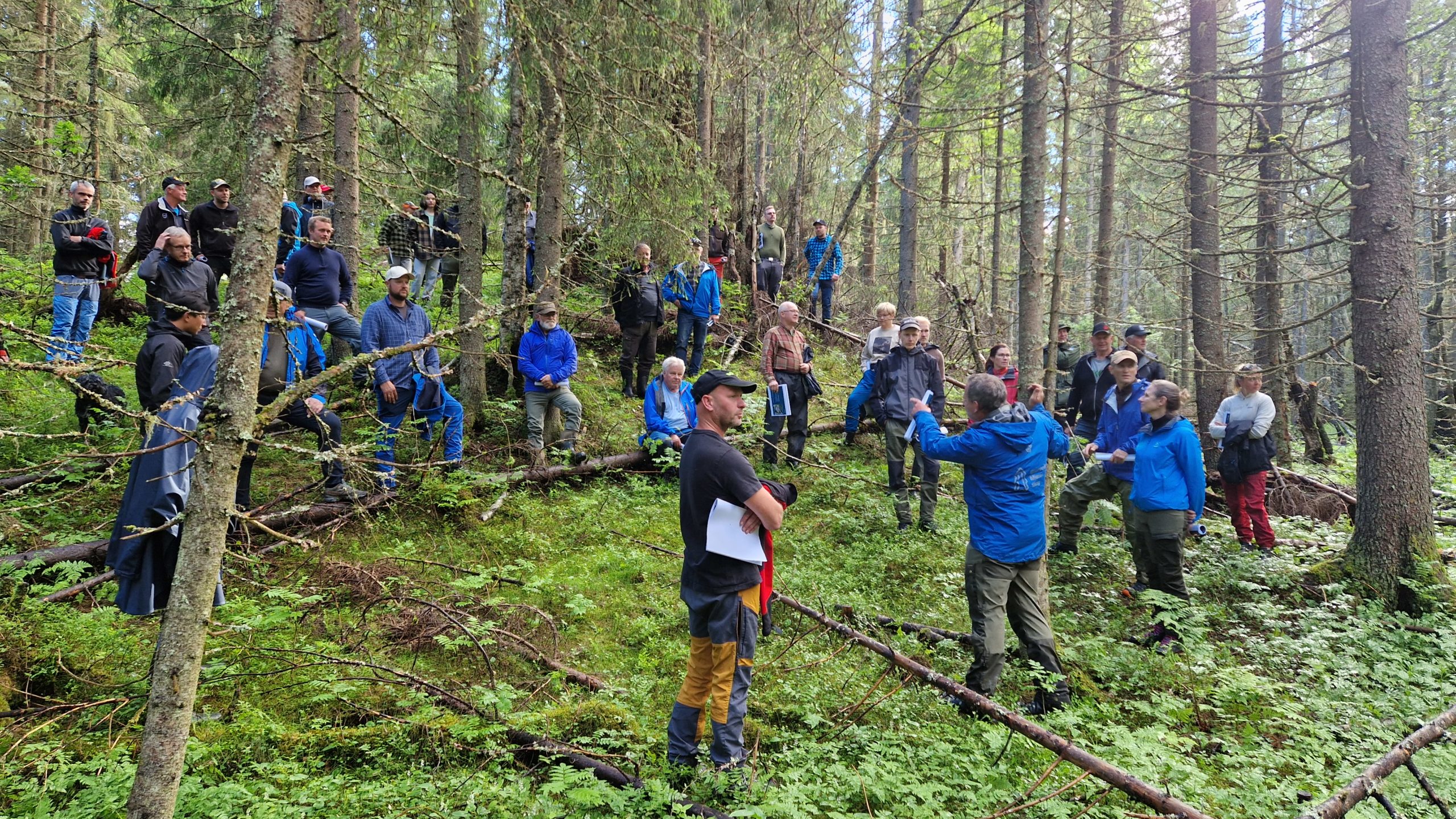 Mann snakker til en stor gruppe mennesker i skogen.