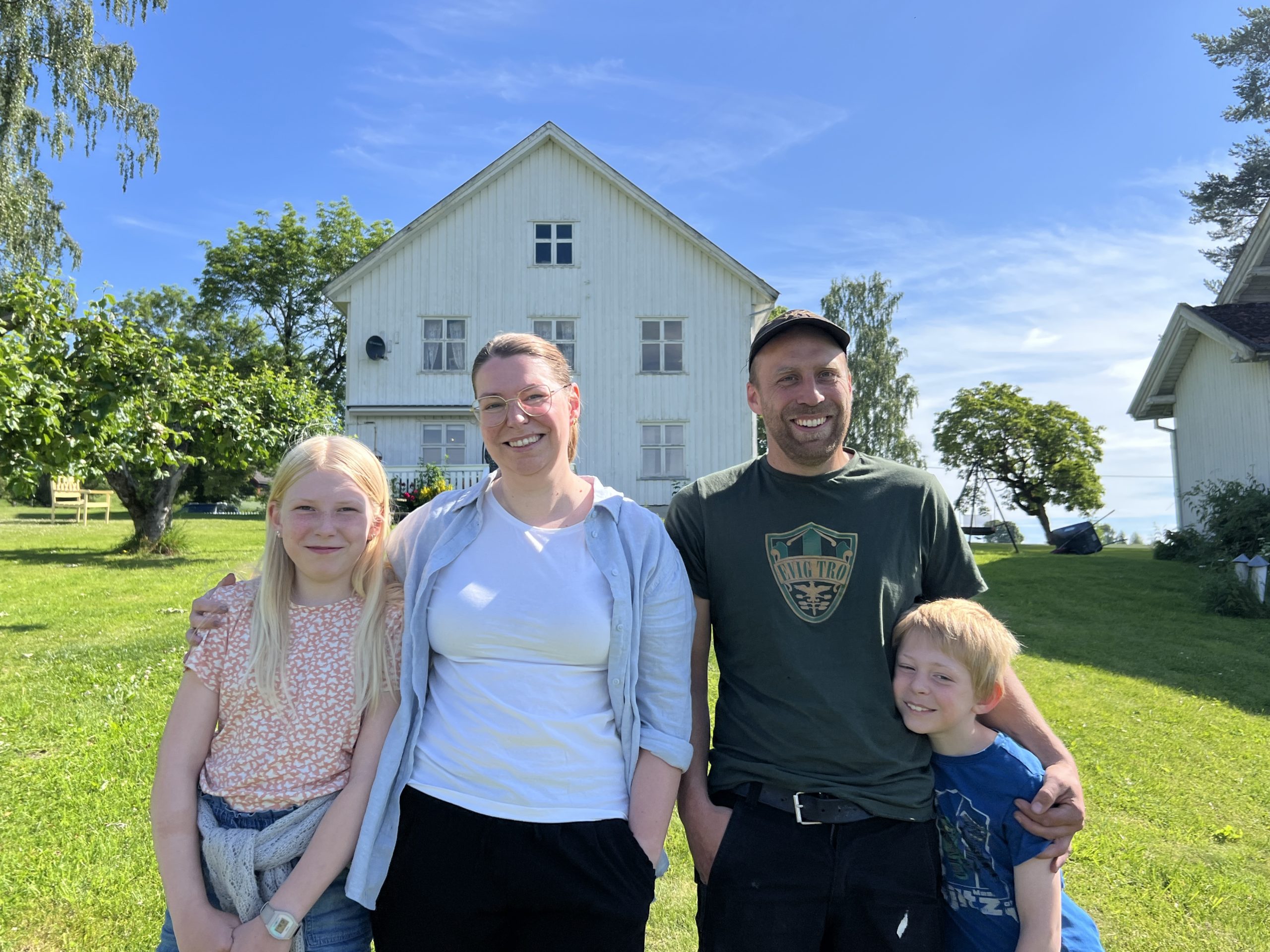 Familie foran gårdsbygning.